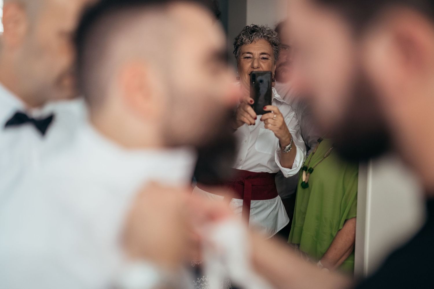Someone taking photos during wedding preparations while others adjust formal attire.