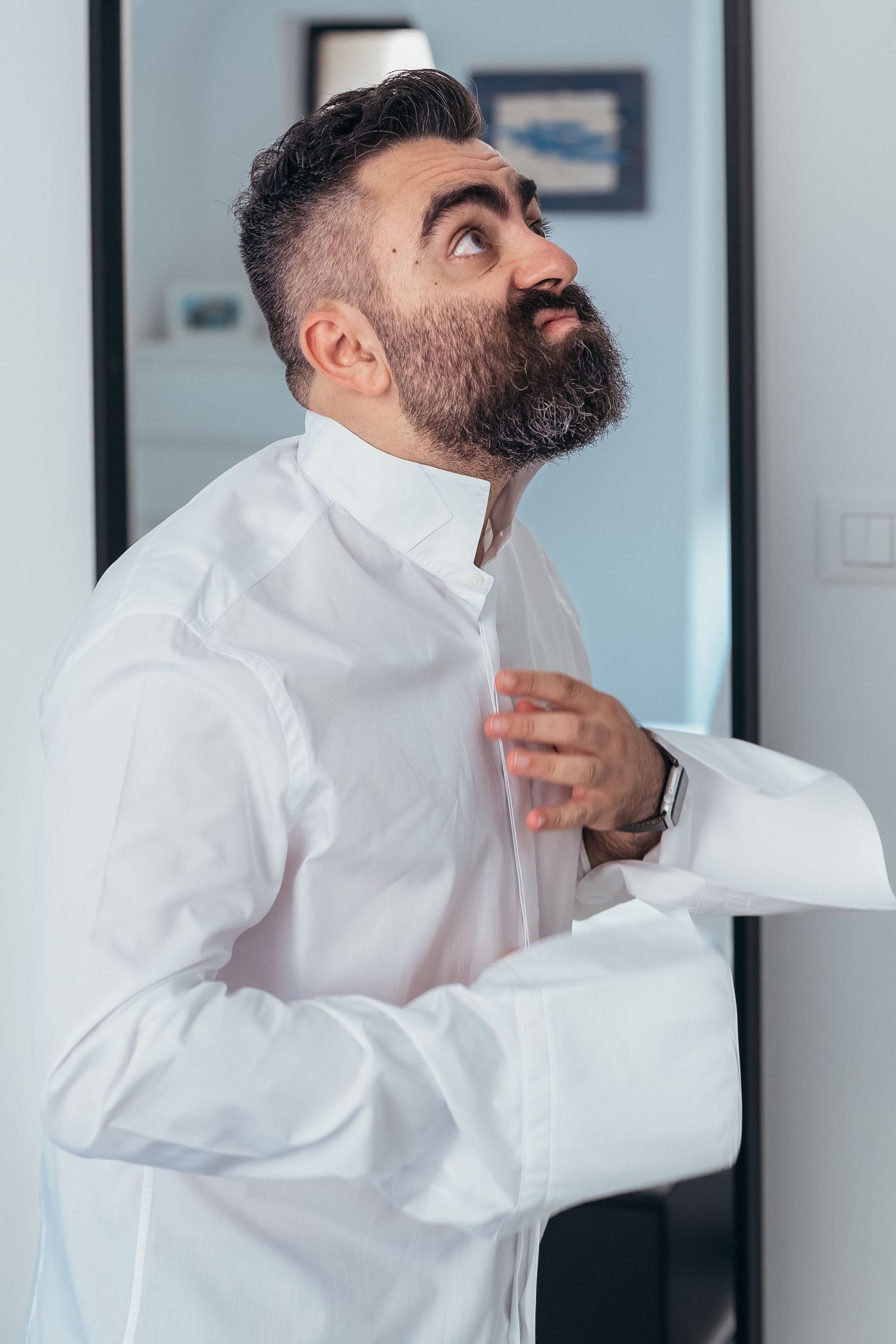Person in white dress shirt adjusting collar while looking up.