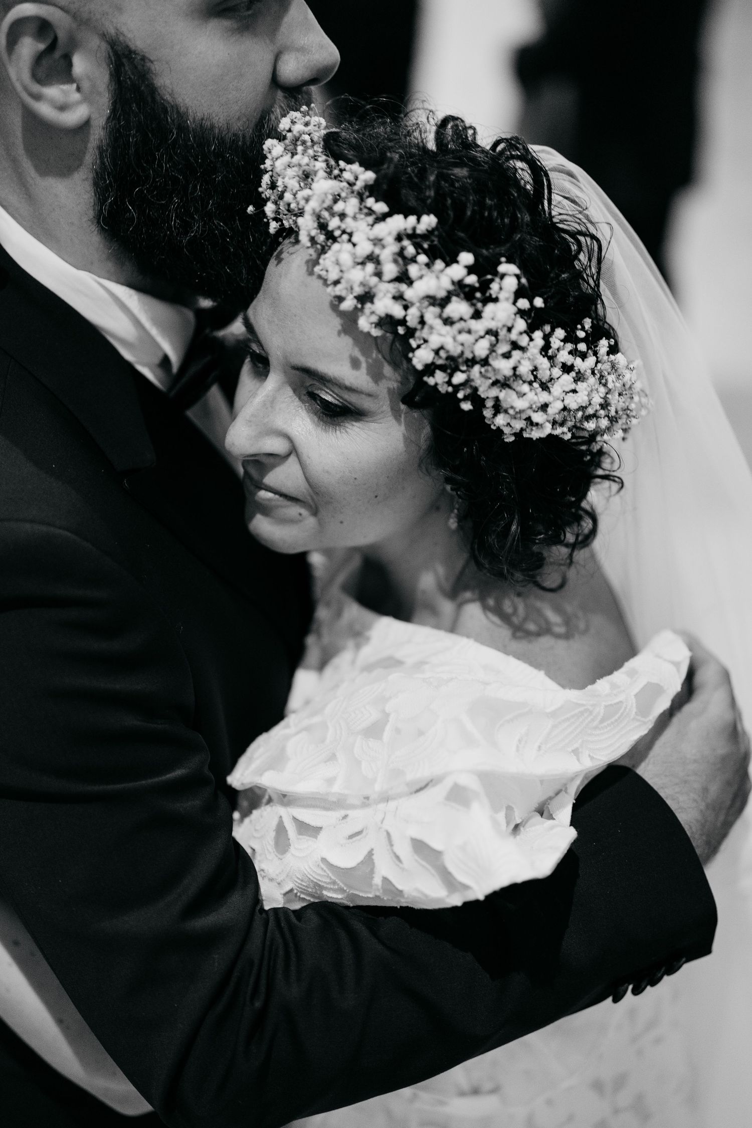 Black and white close-up of wedding couple with delicate floral crown and lace dress details.