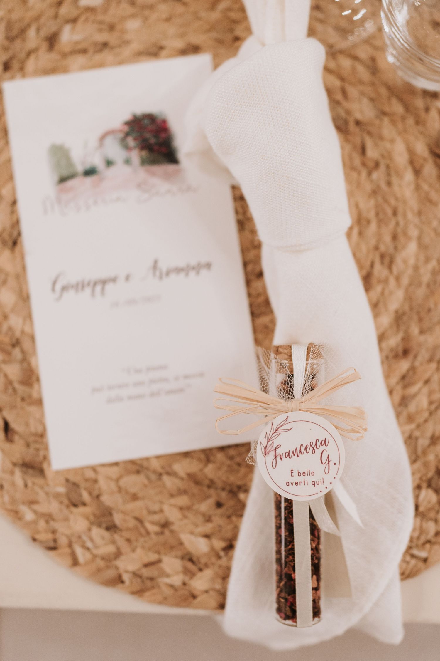 Wedding invitation and favor detail shot on natural woven texture with decorative ribbon.