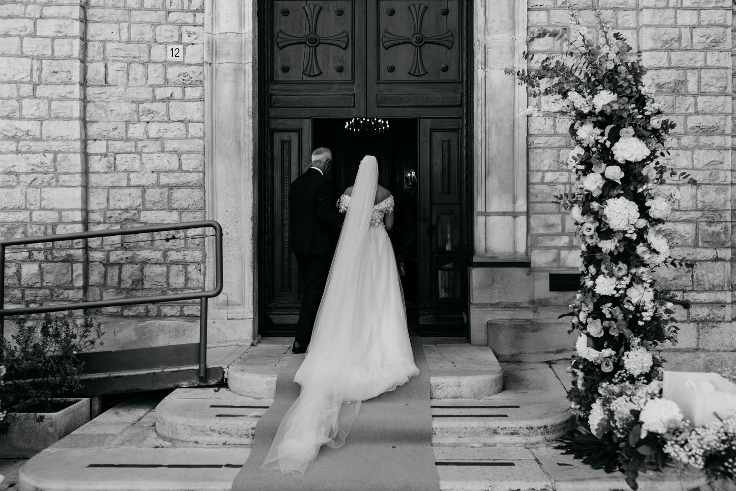 Bridal entrance at stone church with floral arch and elegant doorway.