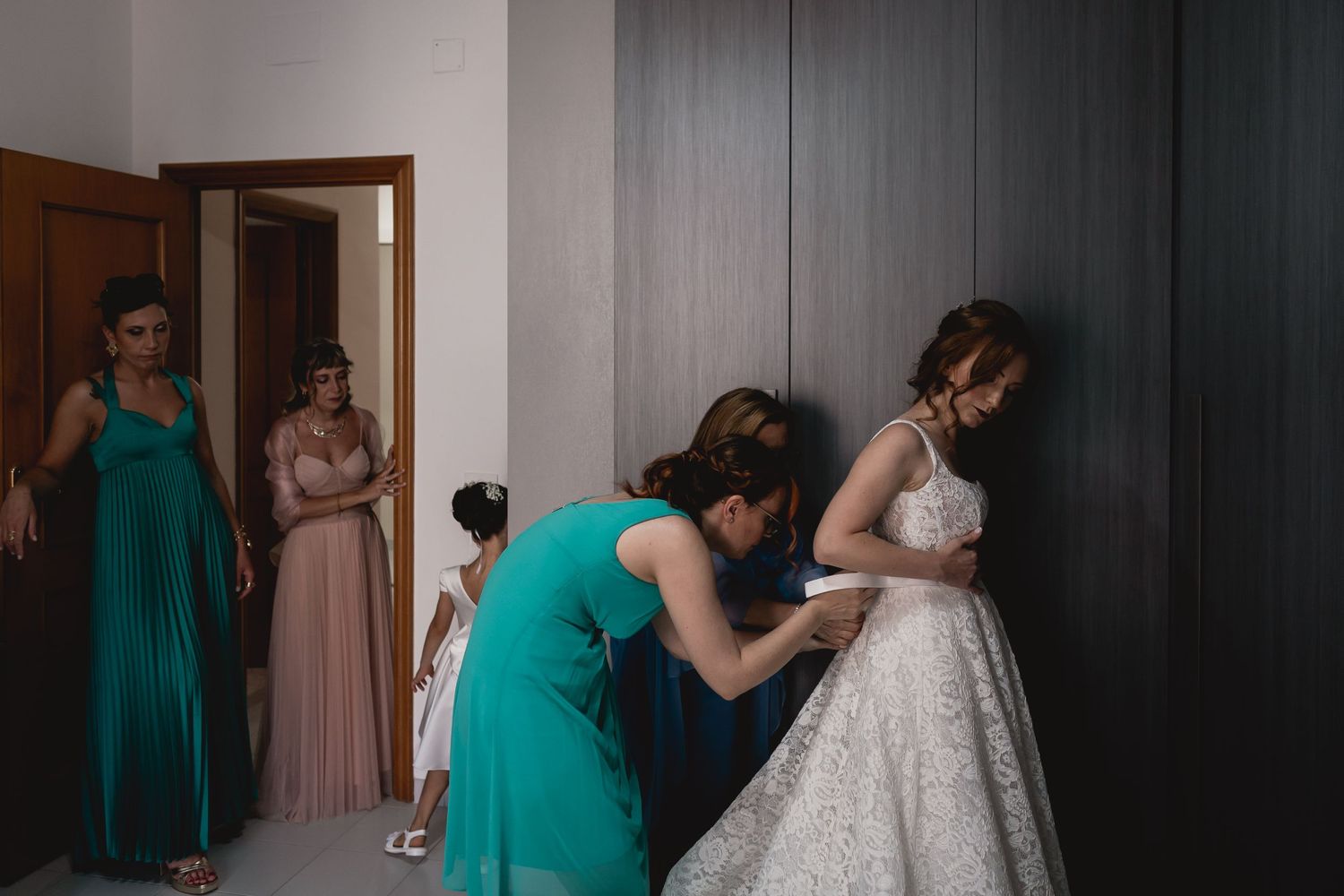 Wedding dress being adjusted by attendants in green and pink dresses.