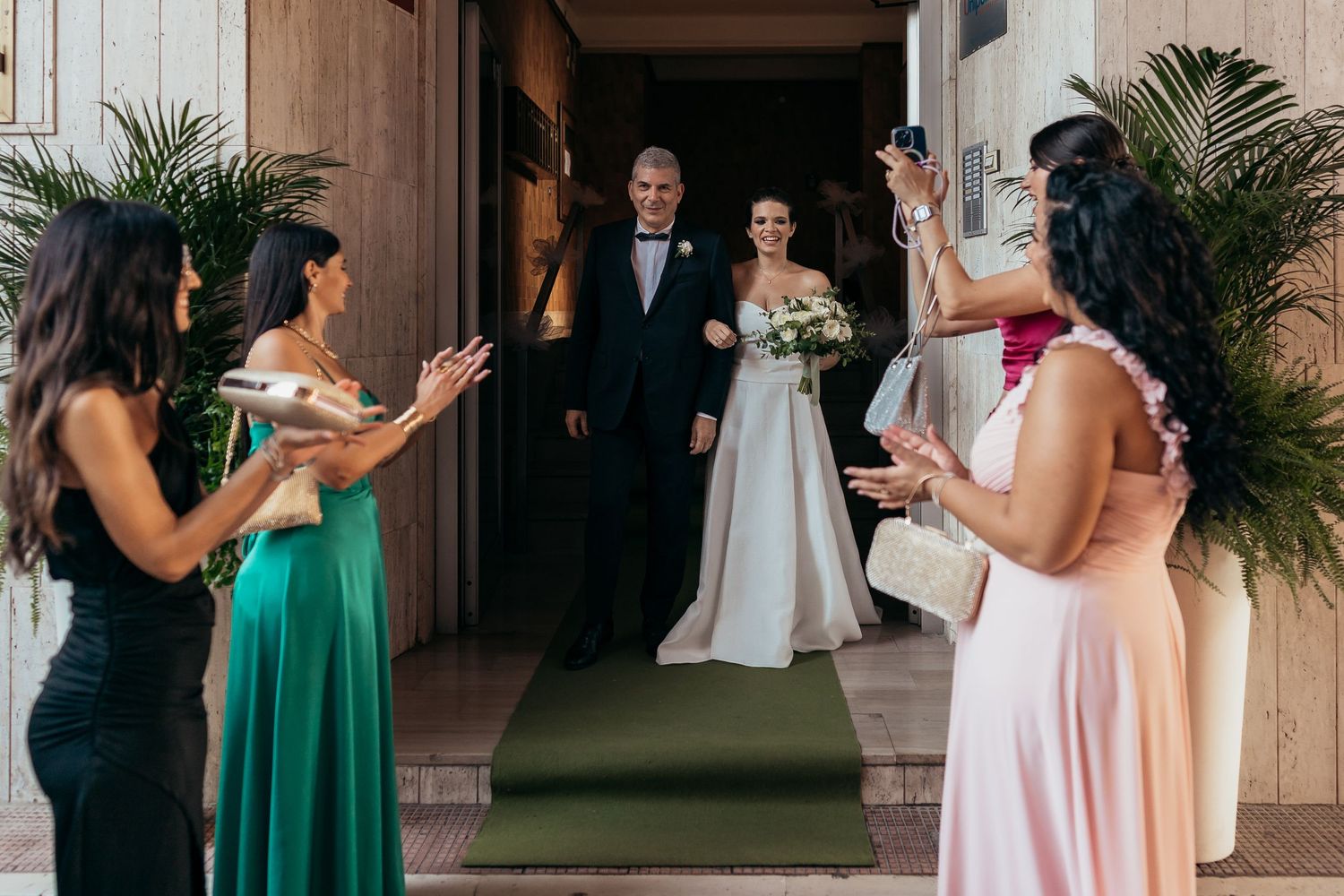 Wedding scene with bridesmaids in colorful dresses welcoming the newlyweds at a church entrance.