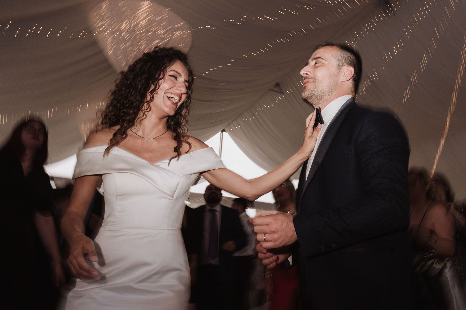 Couple dancing together at wedding reception under string lights.