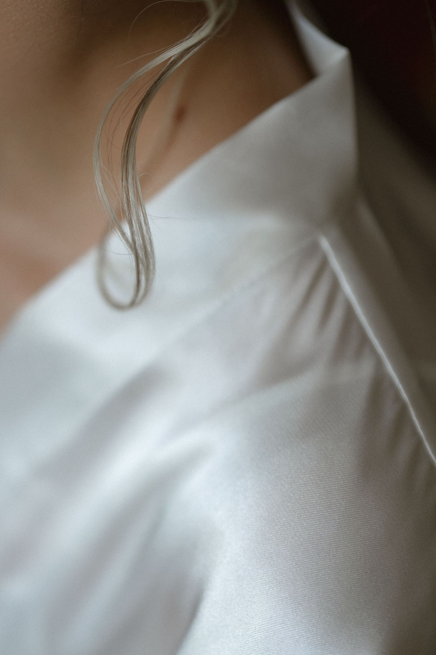 A close-up detail shot of a white satin or silk fabric showing soft folds and texture in natural light.