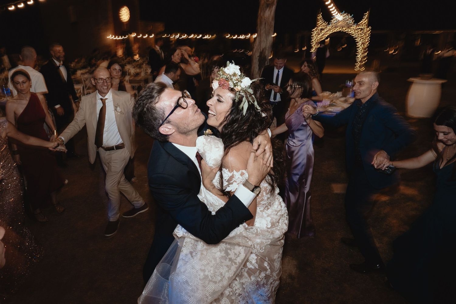 Wedding guests dancing and celebrating on a dimly lit dance floor at a reception party.