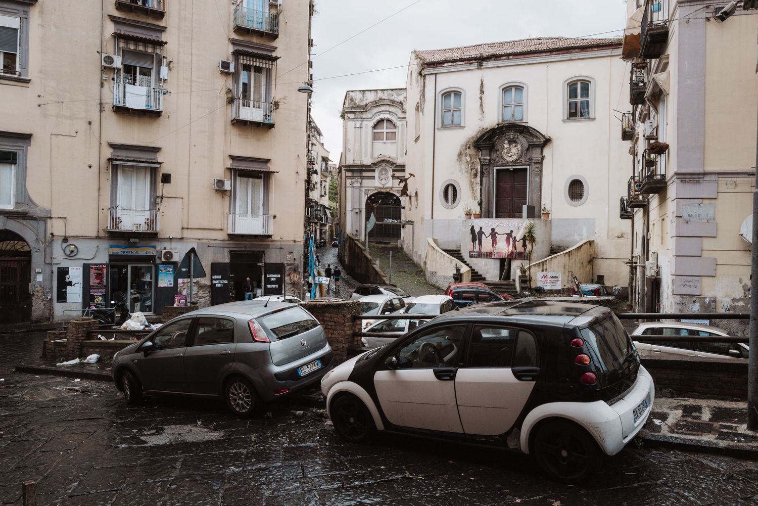 Old European urban street with parked cars and historic buildings in a gritty neighborhood.