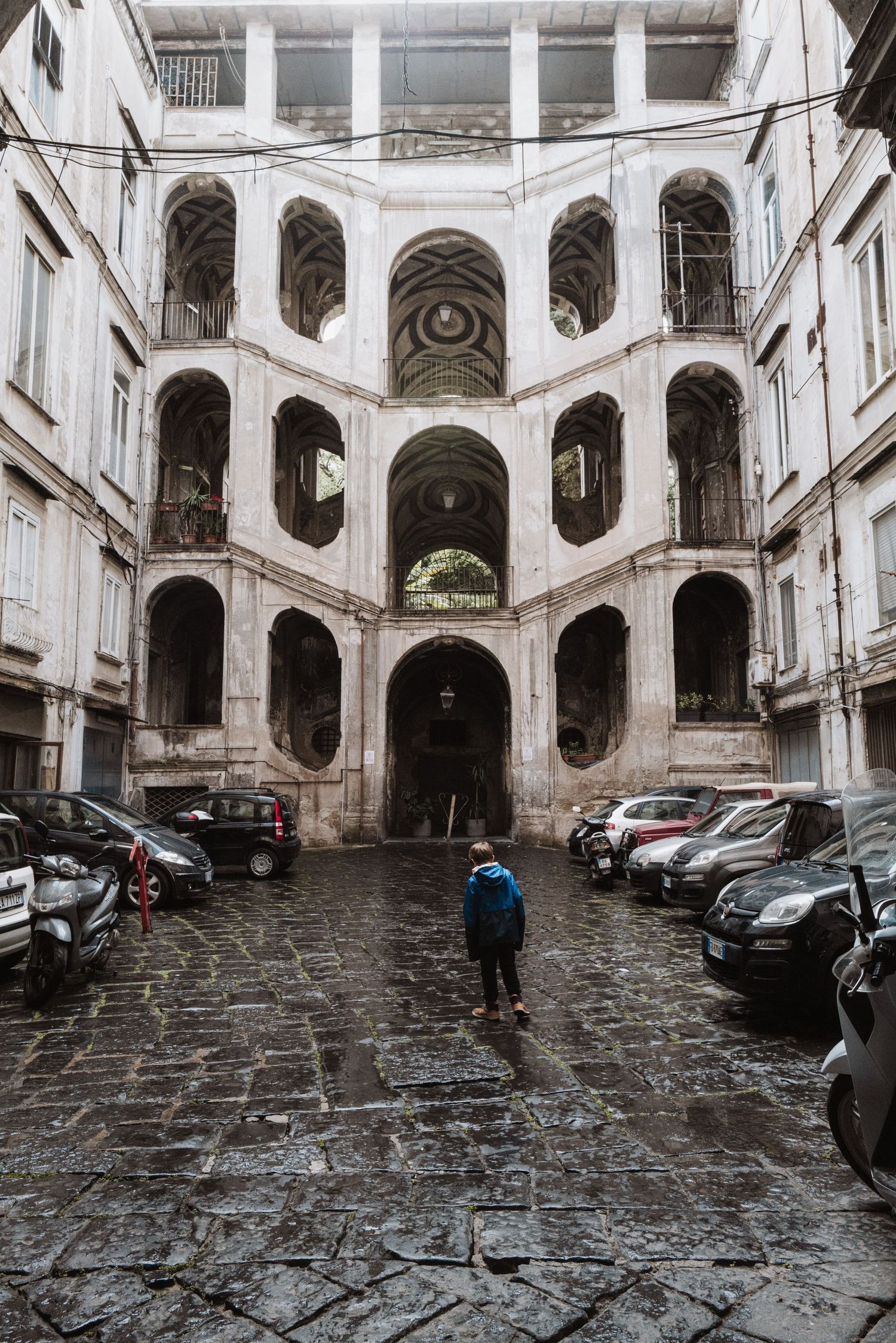 Historic courtyard with spiral archways and parked cars in Naples, Italy.