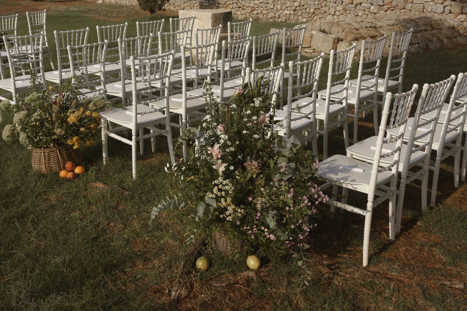 White wooden chairs lined up for outdoor wedding ceremony with rustic floral and pumpkin decorations.