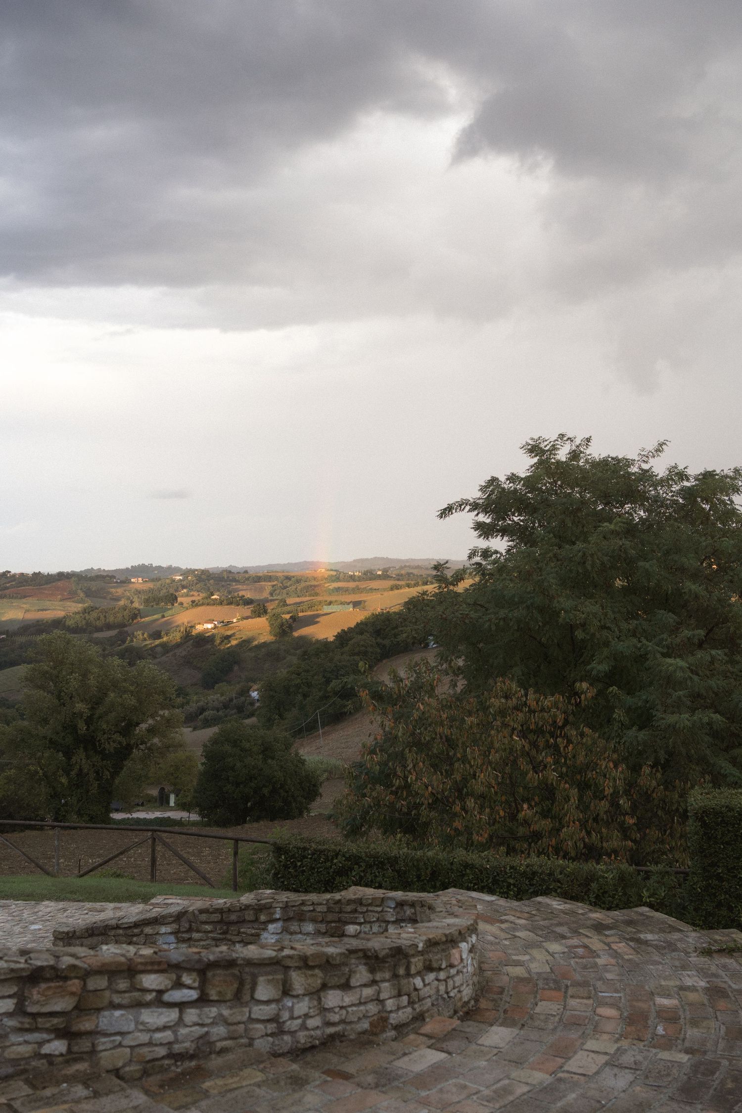 Stone wall overlook with scenic mountain views and cloudy skies at sunset in a rustic countryside setting.