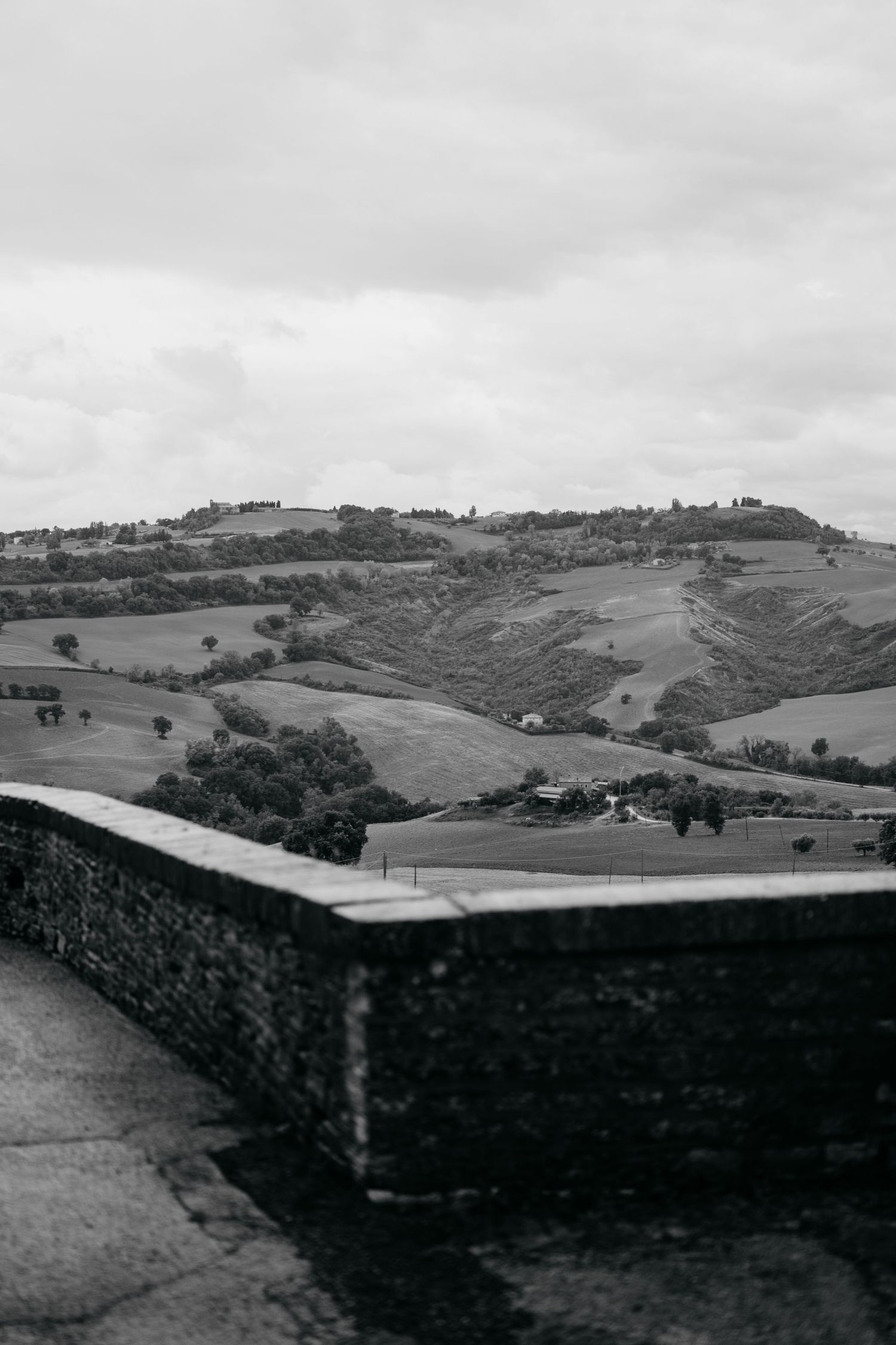 Rolling hills and countryside landscape with stone wall in foreground under cloudy skies.