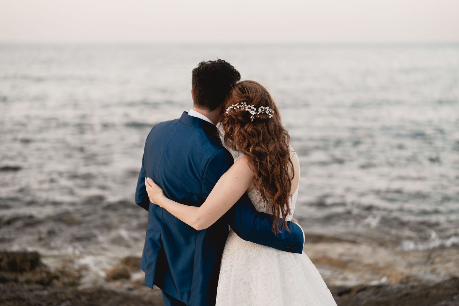 Couple in wedding attire looking out over the ocean together.