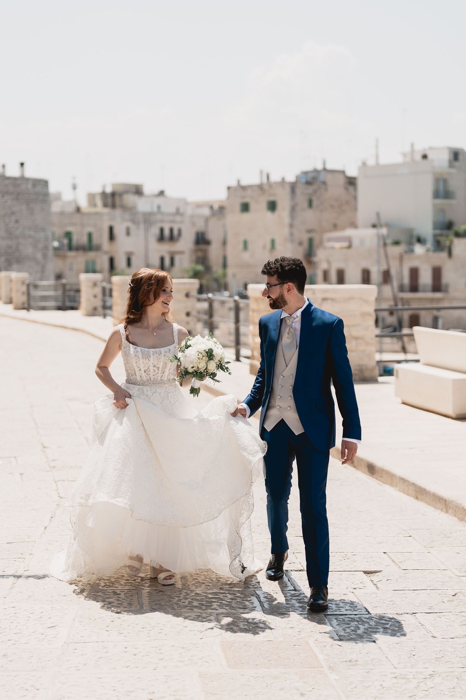 Couple walking through sun-drenched Mediterranean town streets during wedding photoshoot.