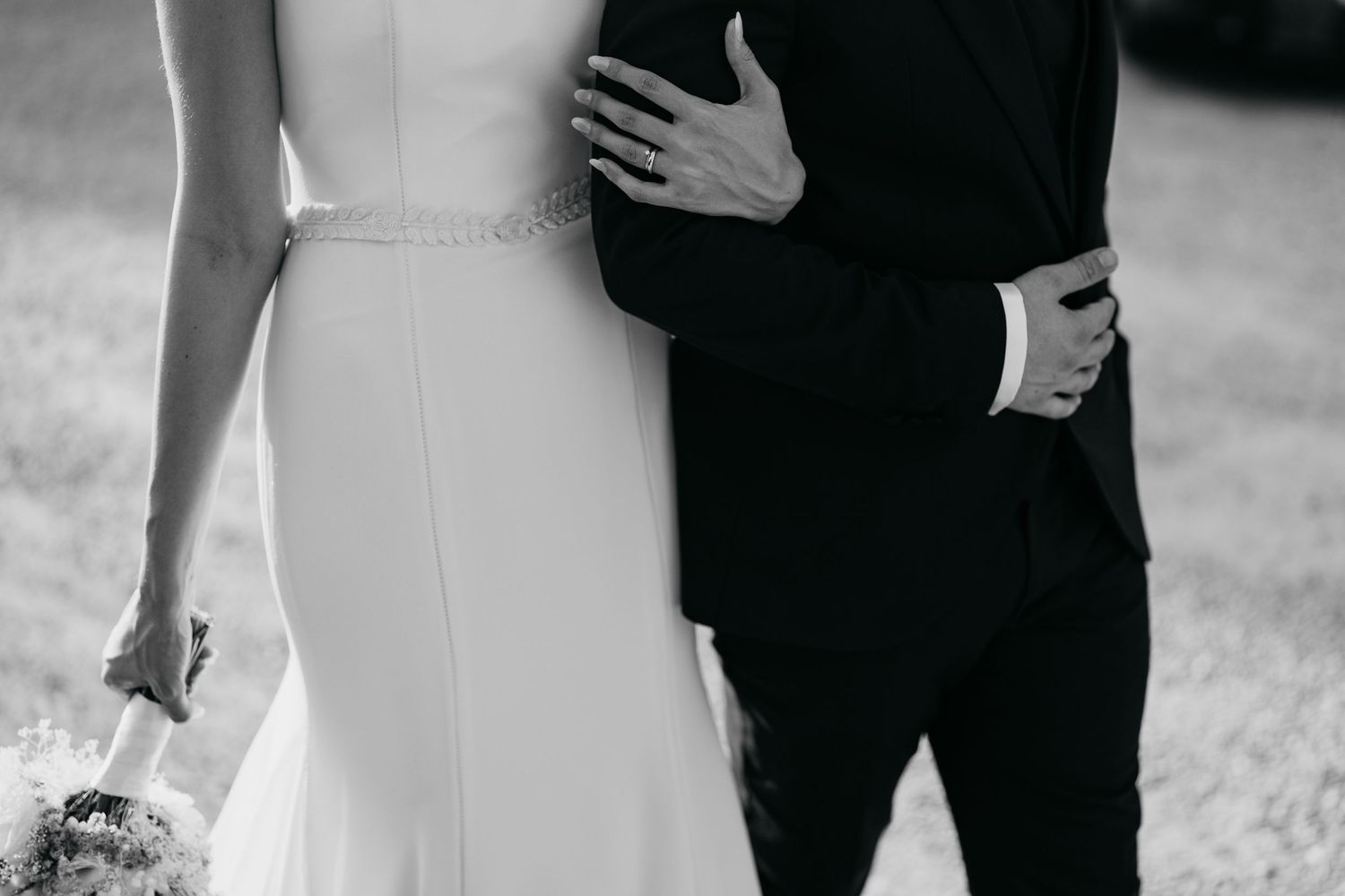 Black and white close-up of a couple embracing at their wedding, with the bride holding a small bouquet.