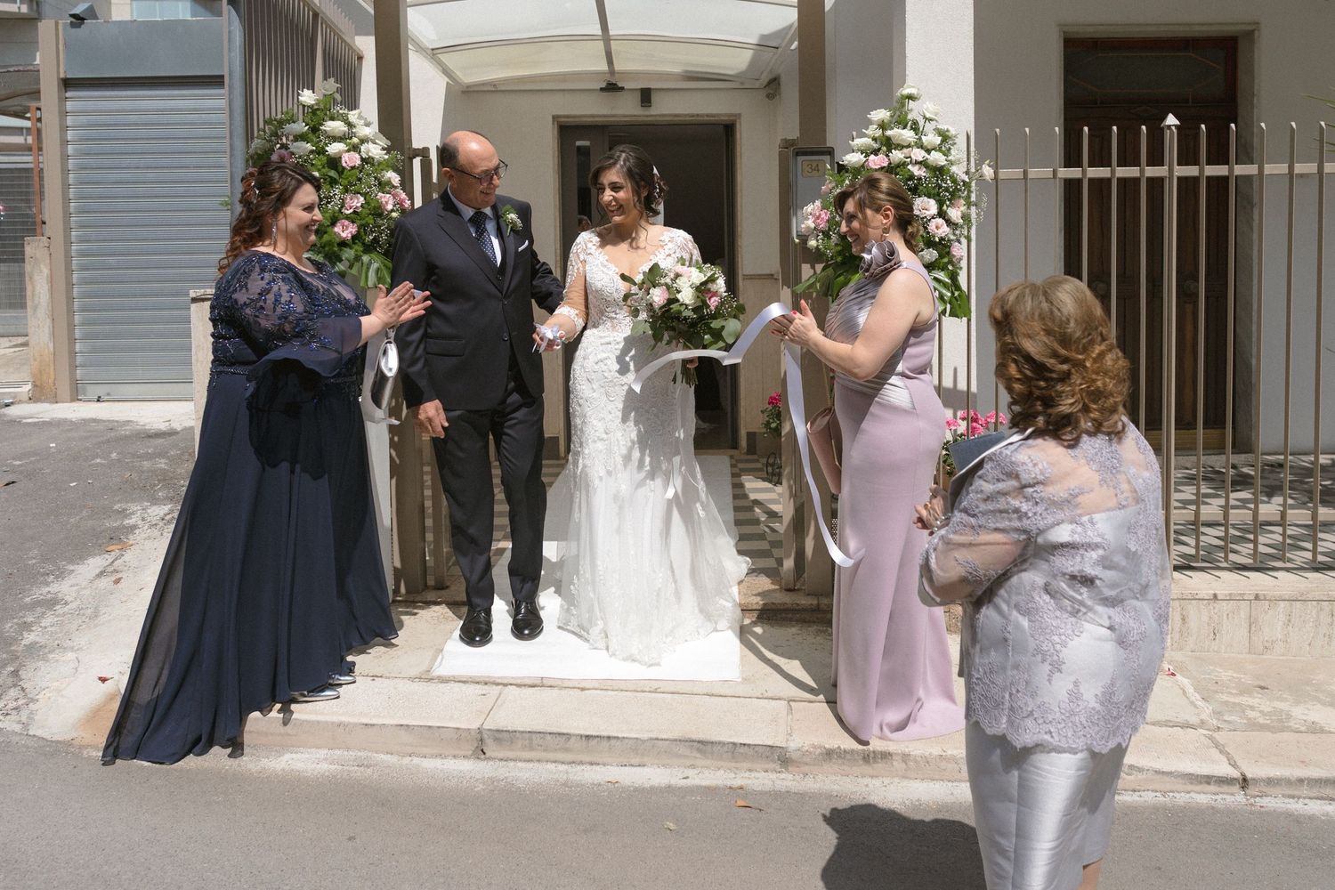 Wedding party gathered on outdoor steps for photos with floral arrangements.