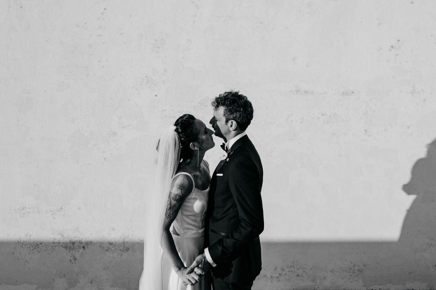 Artistic black and white silhouette of newlyweds against white wall.