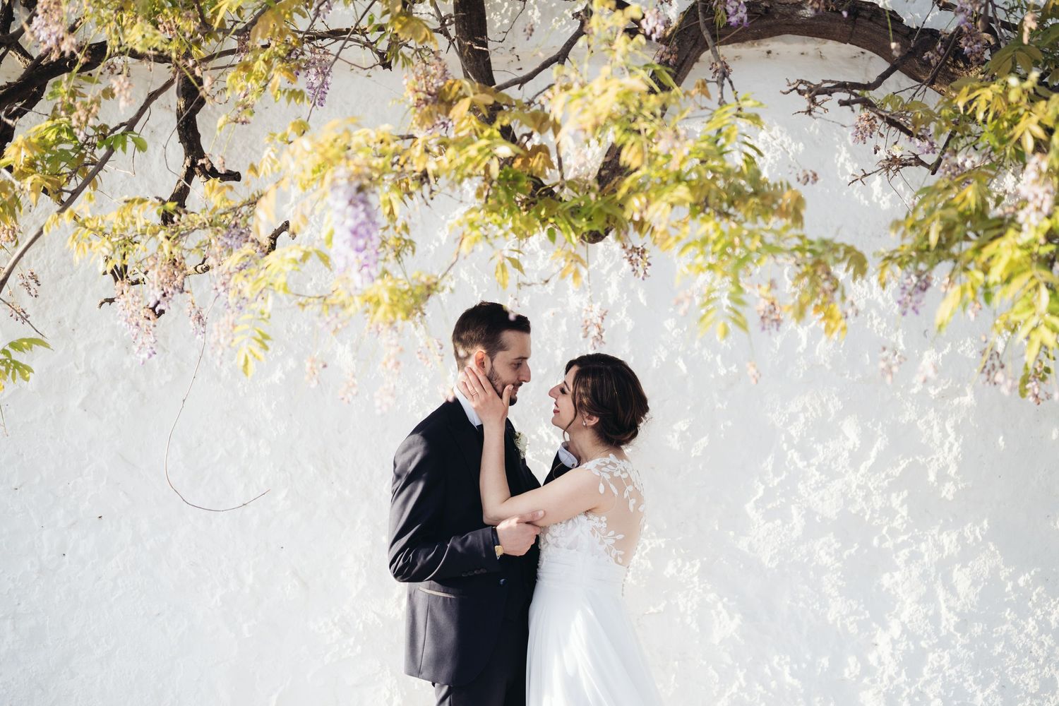 Newlyweds sharing an intimate moment under blooming yellow tree branches.