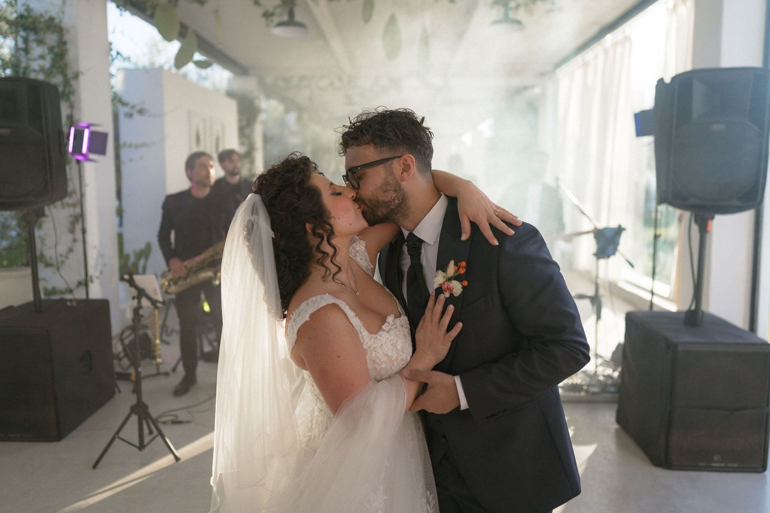 Bride and groom sharing a passionate first kiss surrounded by dramatic smoke effects indoors.