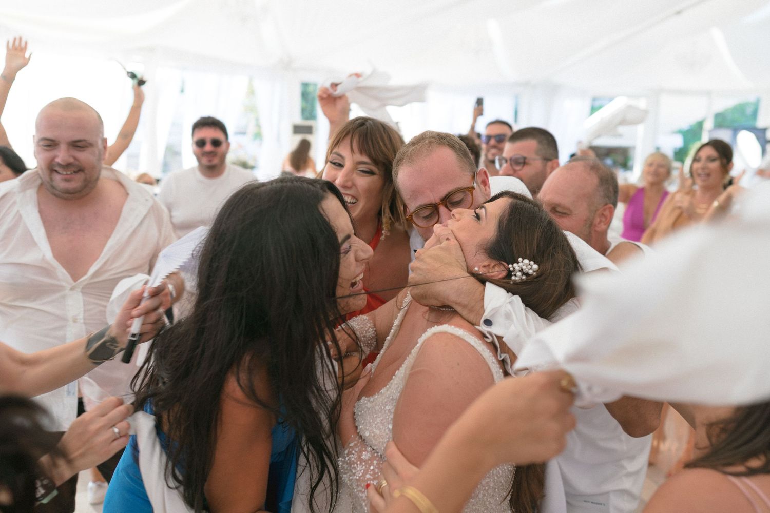 Wedding reception guests dancing and celebrating with joyful energy under a white tent.