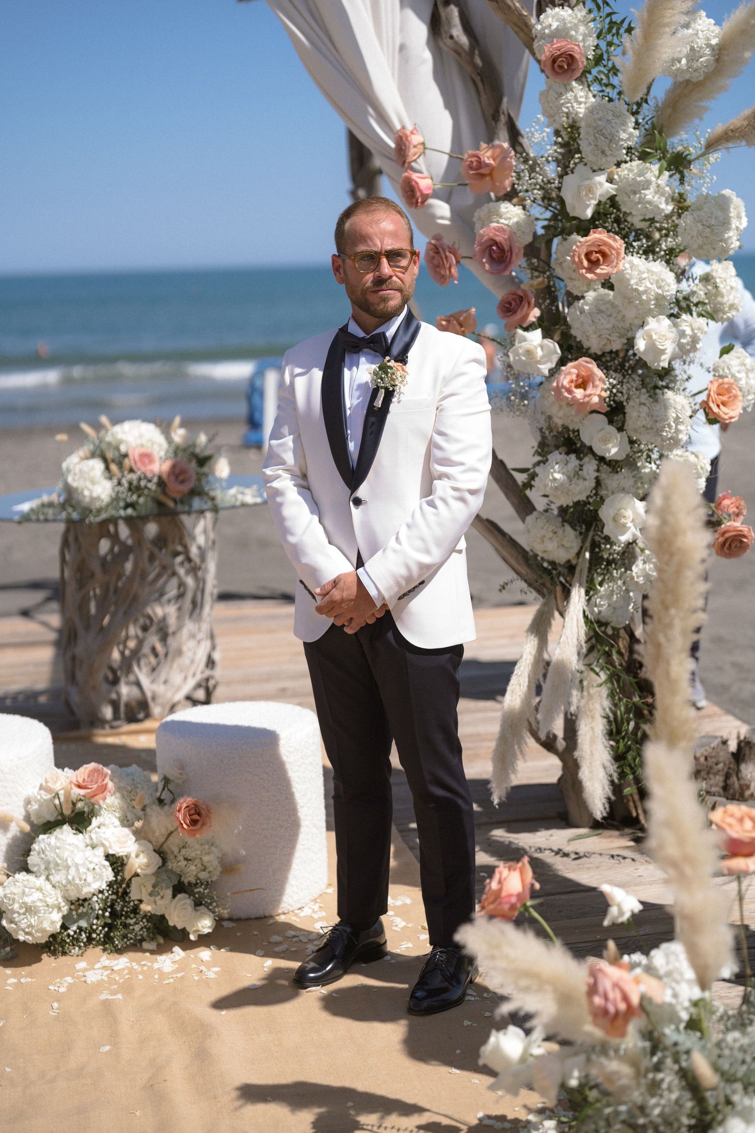 Beach wedding ceremony setup with white floral arrangements and decorative elements on the sand.