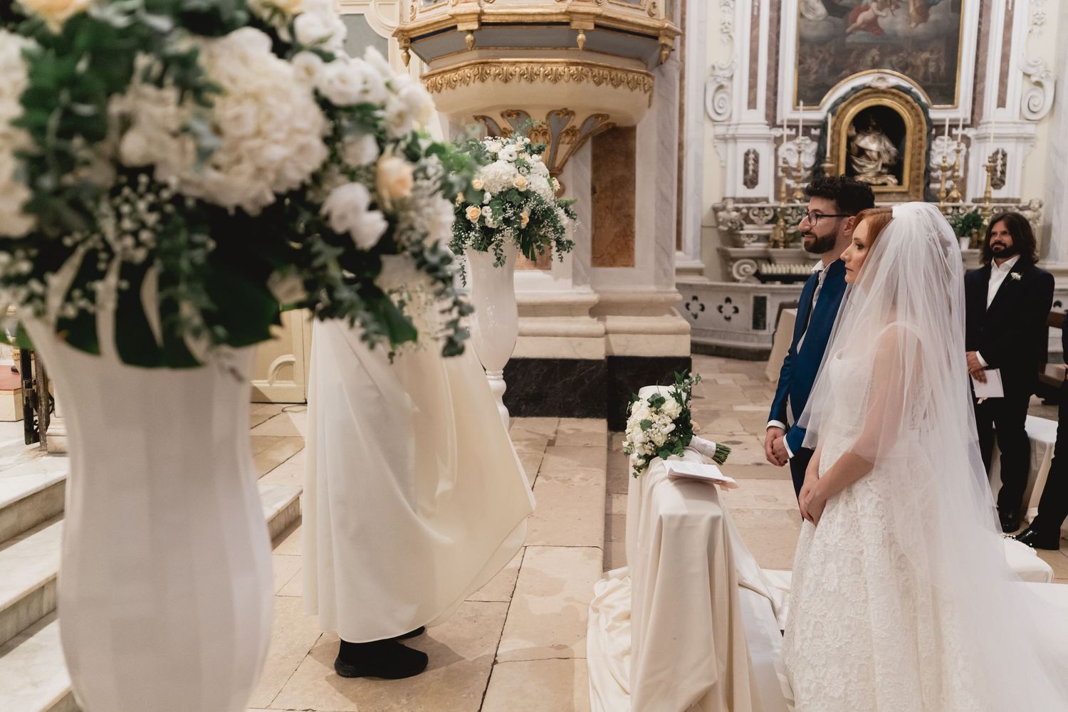 Wedding ceremony setup with white floral arrangements in elegant church setting.