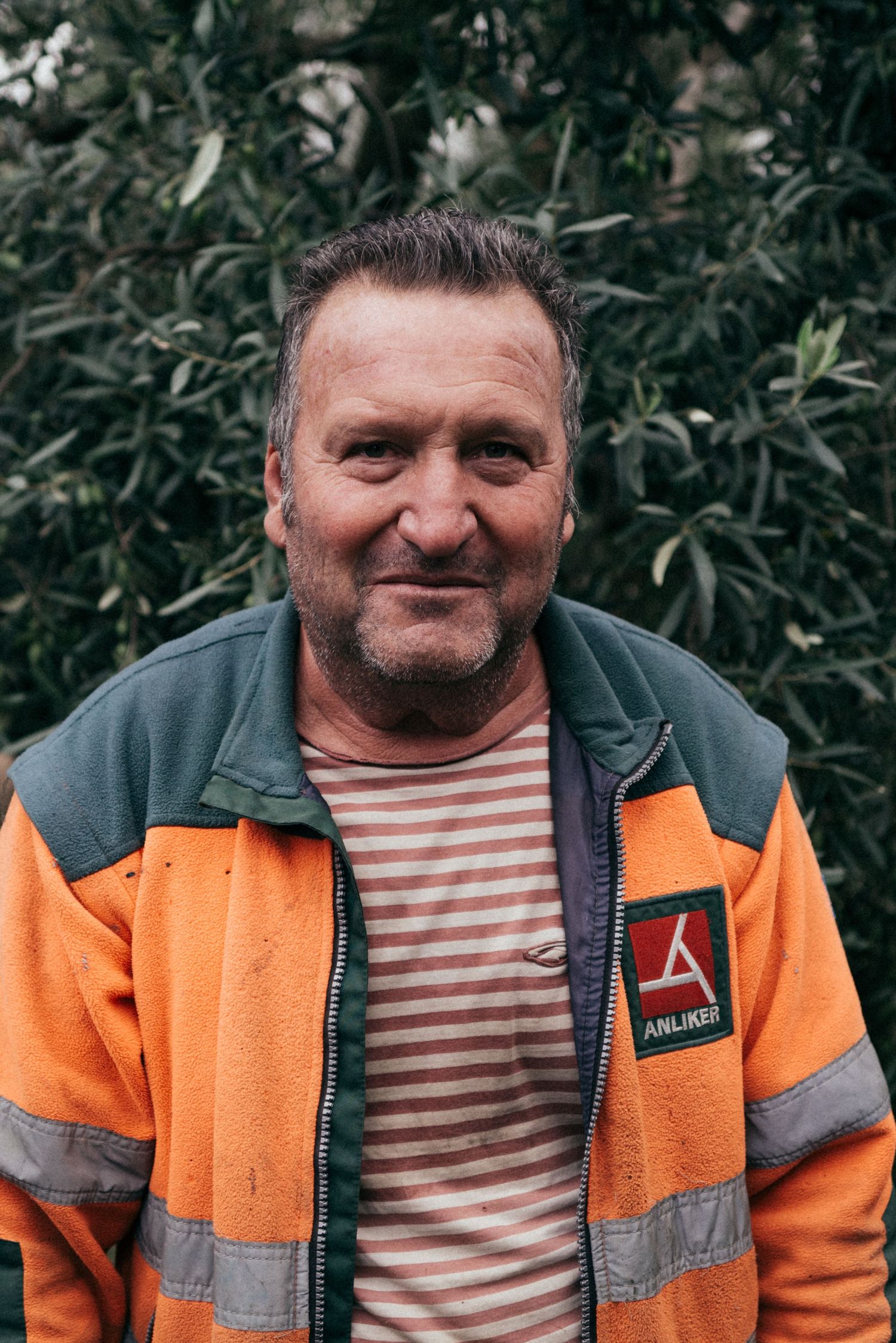 Worker wearing an orange and blue high-visibility uniform with reflective stripes smiles at the camera.