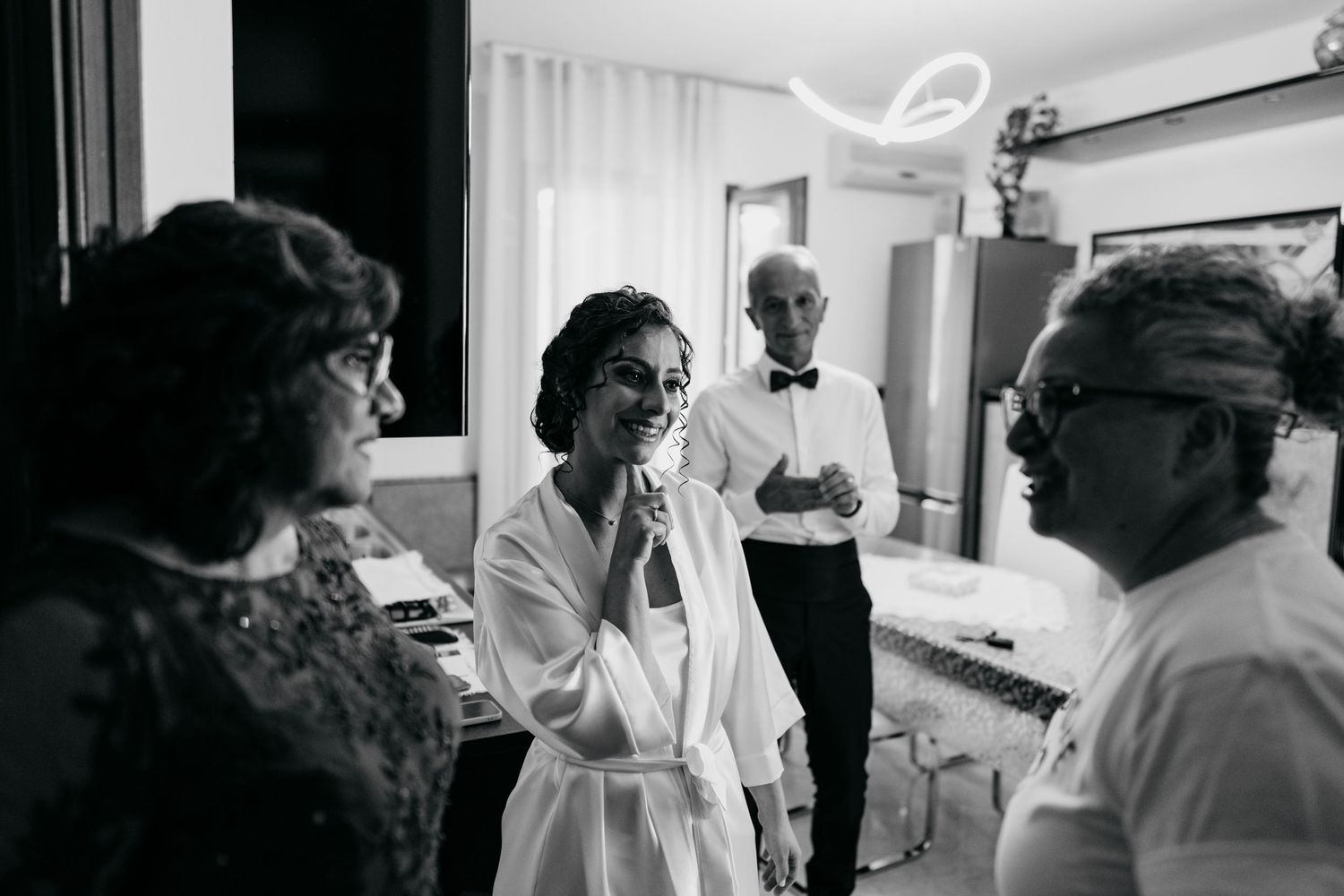 Black and white candid moment of wedding preparation with people in formal attire.