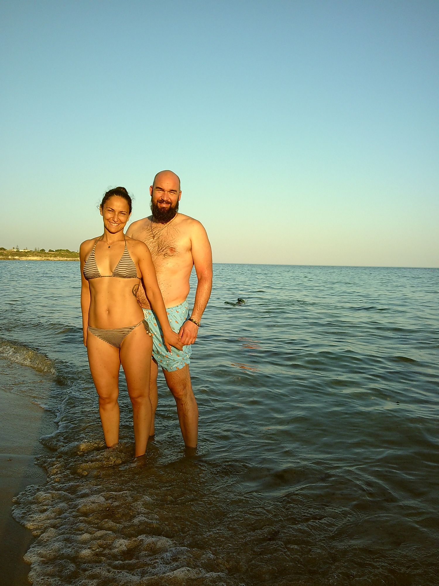 Two beachgoers standing in shallow ocean water during sunset.