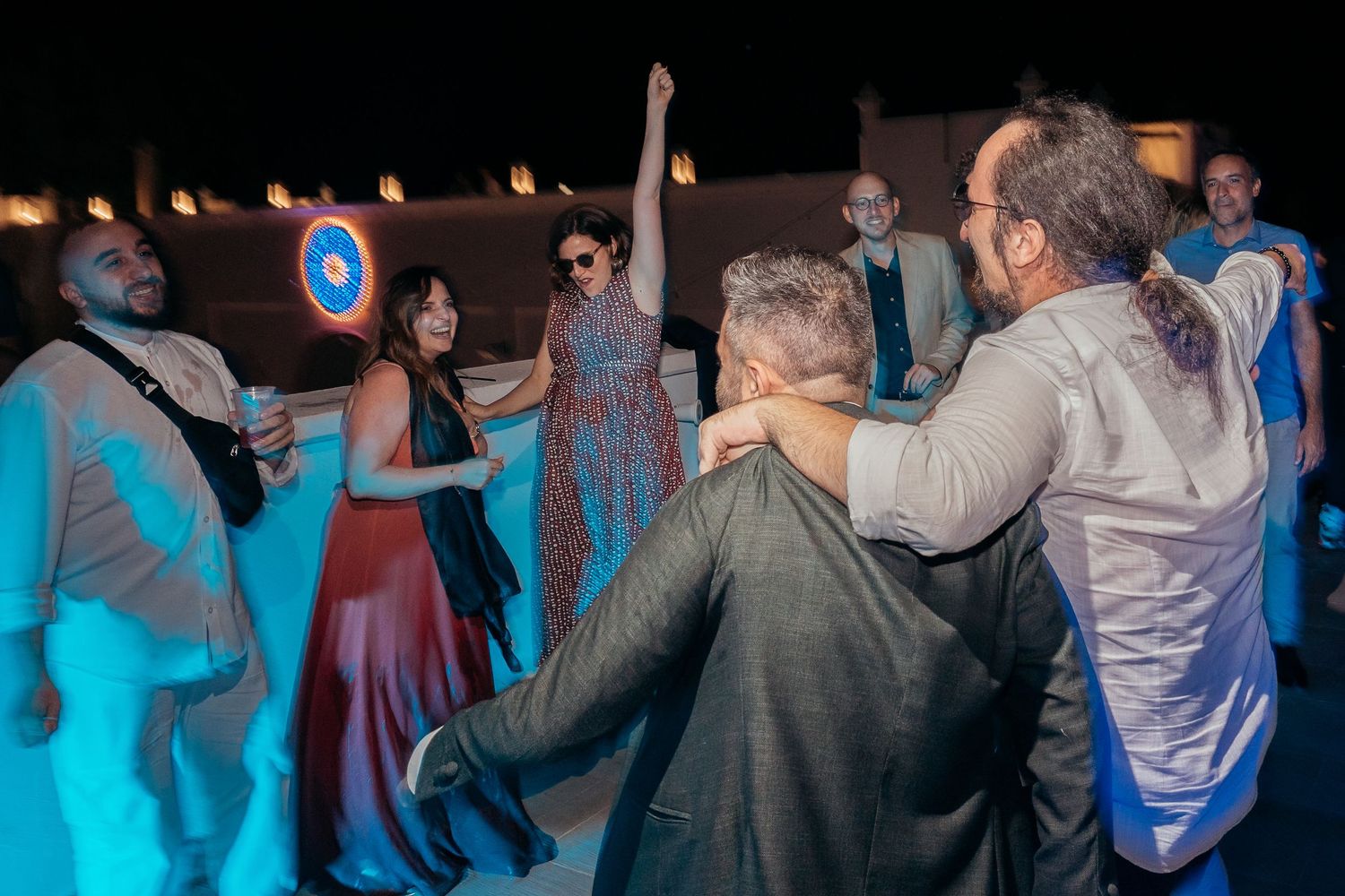 Wedding guests dancing and celebrating on an illuminated outdoor dance floor.