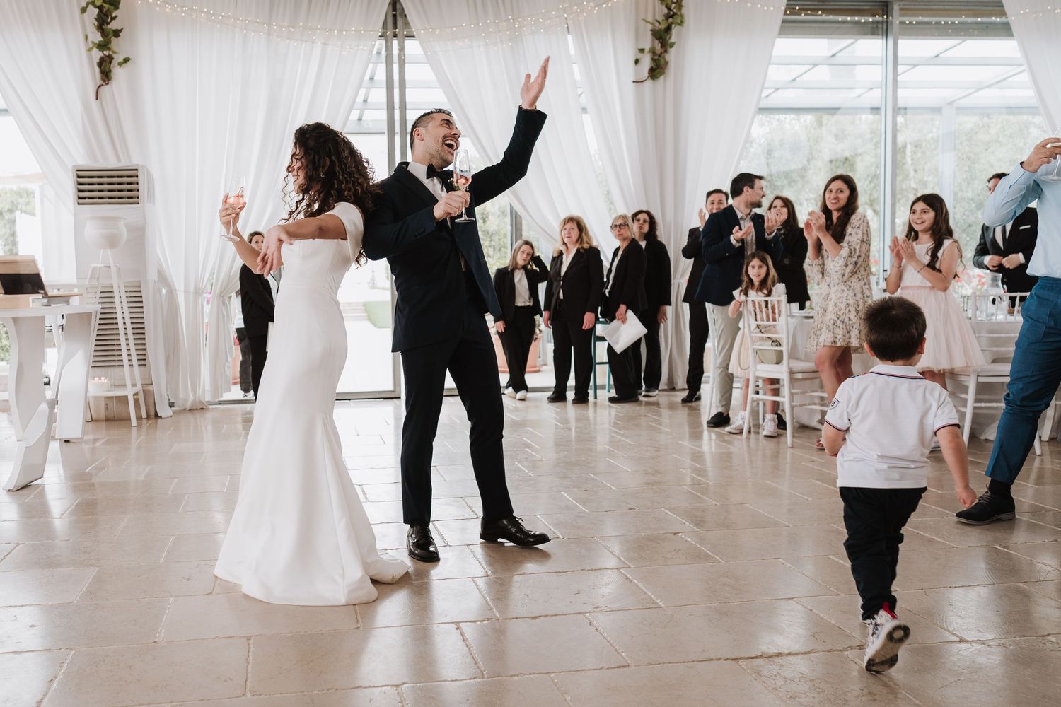 Joyful celebration during a wedding reception in a bright, white-draped venue.