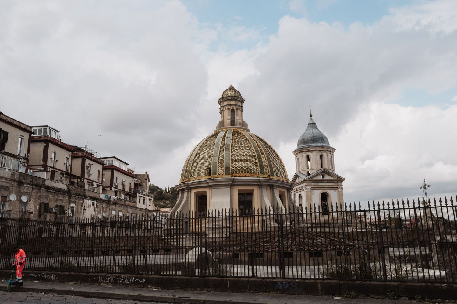 Historic domed church building with ornate architecture behind metal fencing on an overcast day.