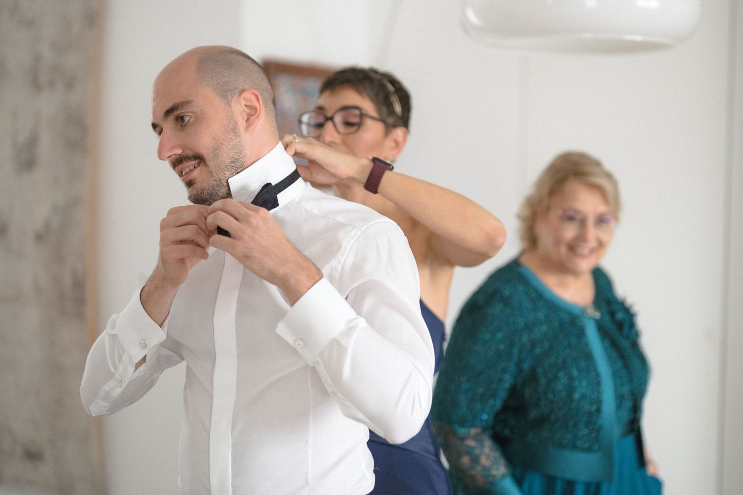 Wedding party members in formal attire adjusting their ties and getting ready in a bright room.