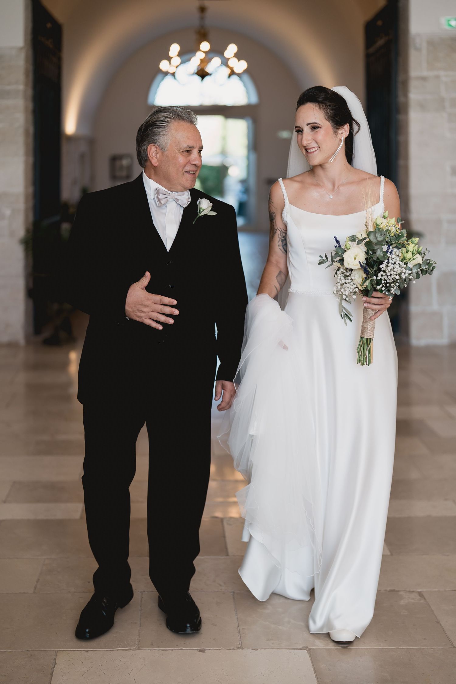 A wedding party member walks down a hallway with someone in traditional wedding attire.