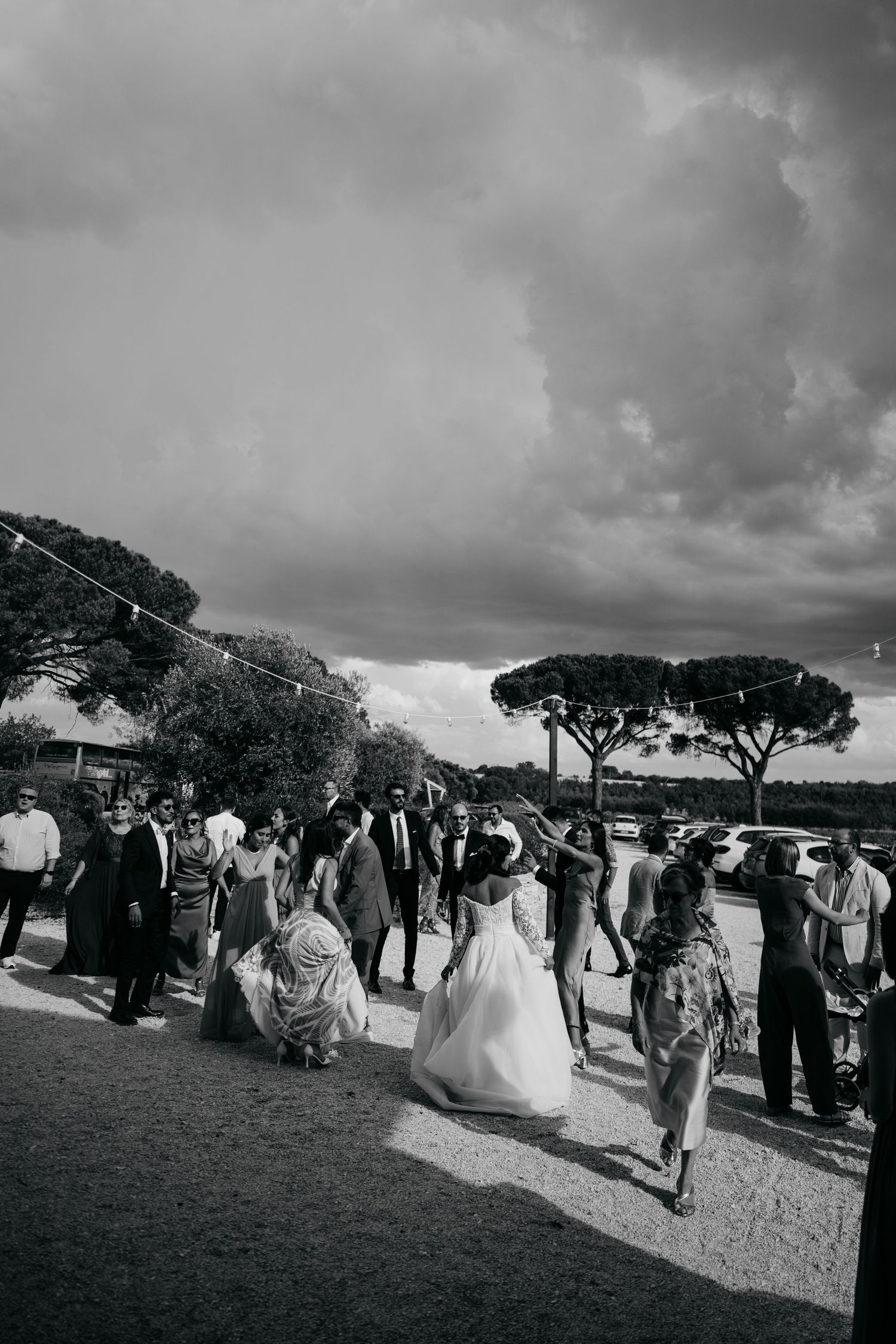 Black and white panoramic shot of wedding guests gathering outdoors under dramatic clouds.