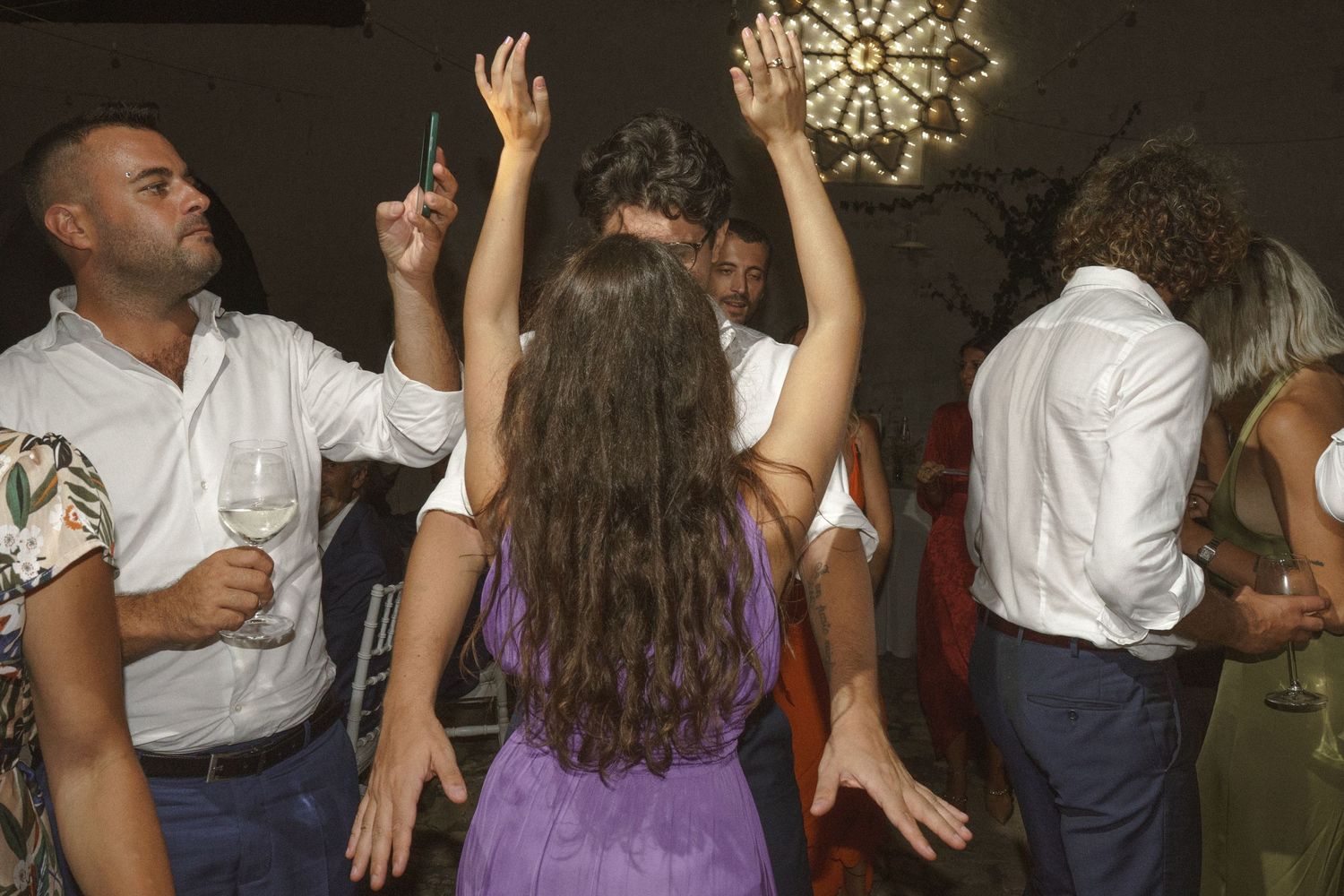 People dancing and celebrating with raised arms at a lively wedding reception.
