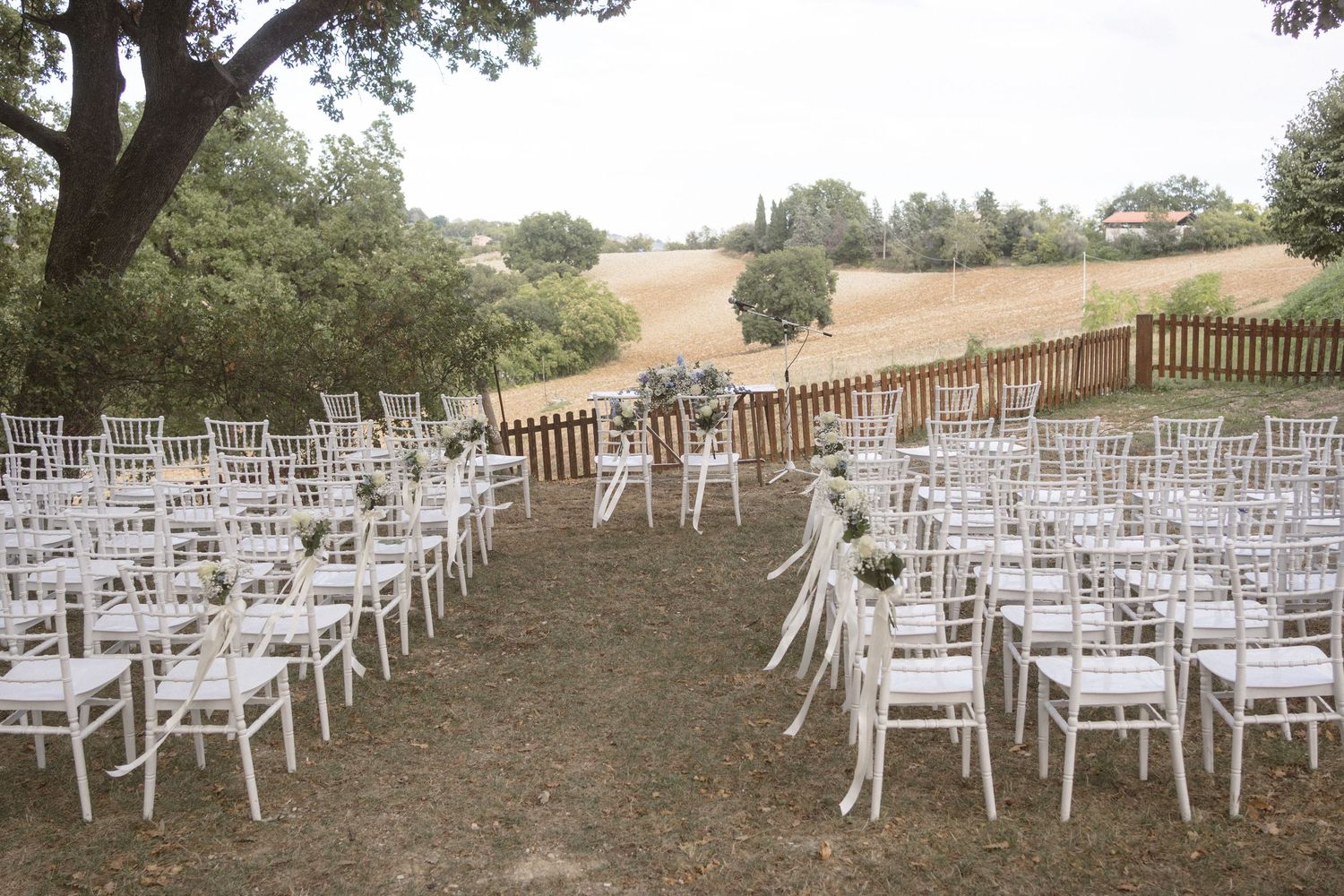 Rows of empty white chairs set up for an outdoor ceremony on a hillside.