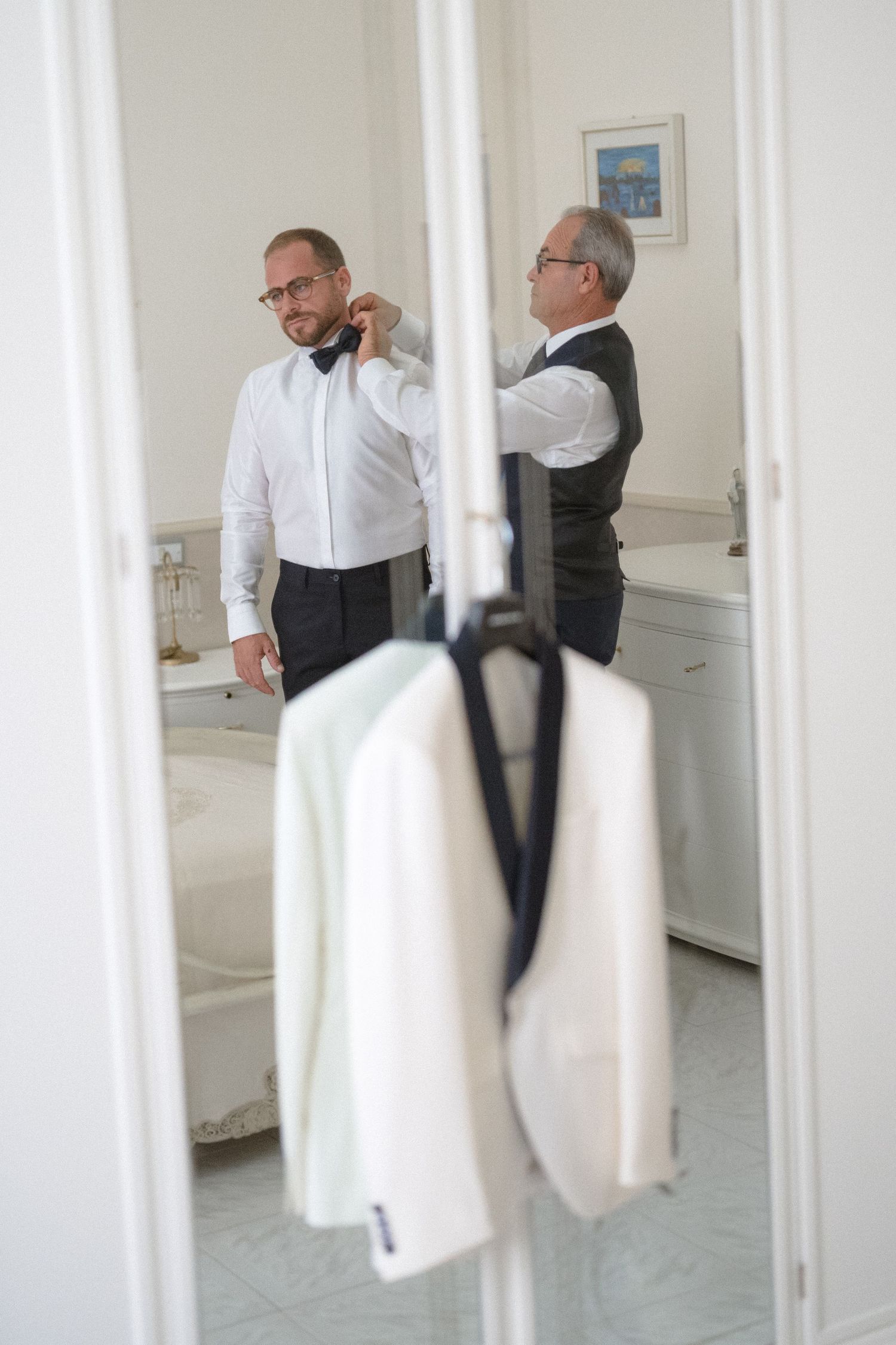Wedding party members in formal attire seen through white doorway frames.