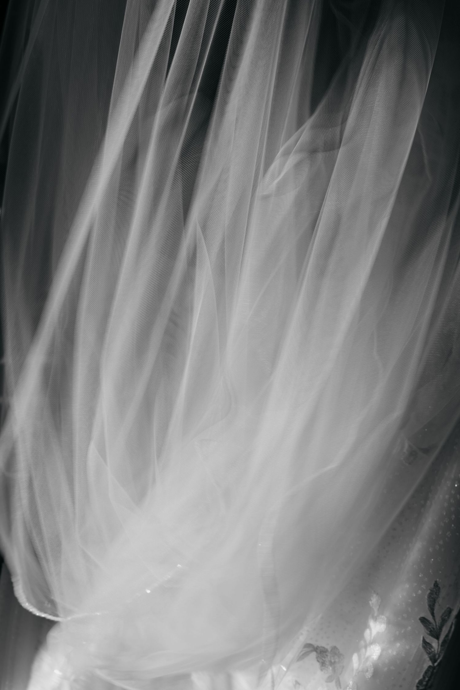 Close-up black and white detail shot of flowing bridal veil with delicate lace embroidery.