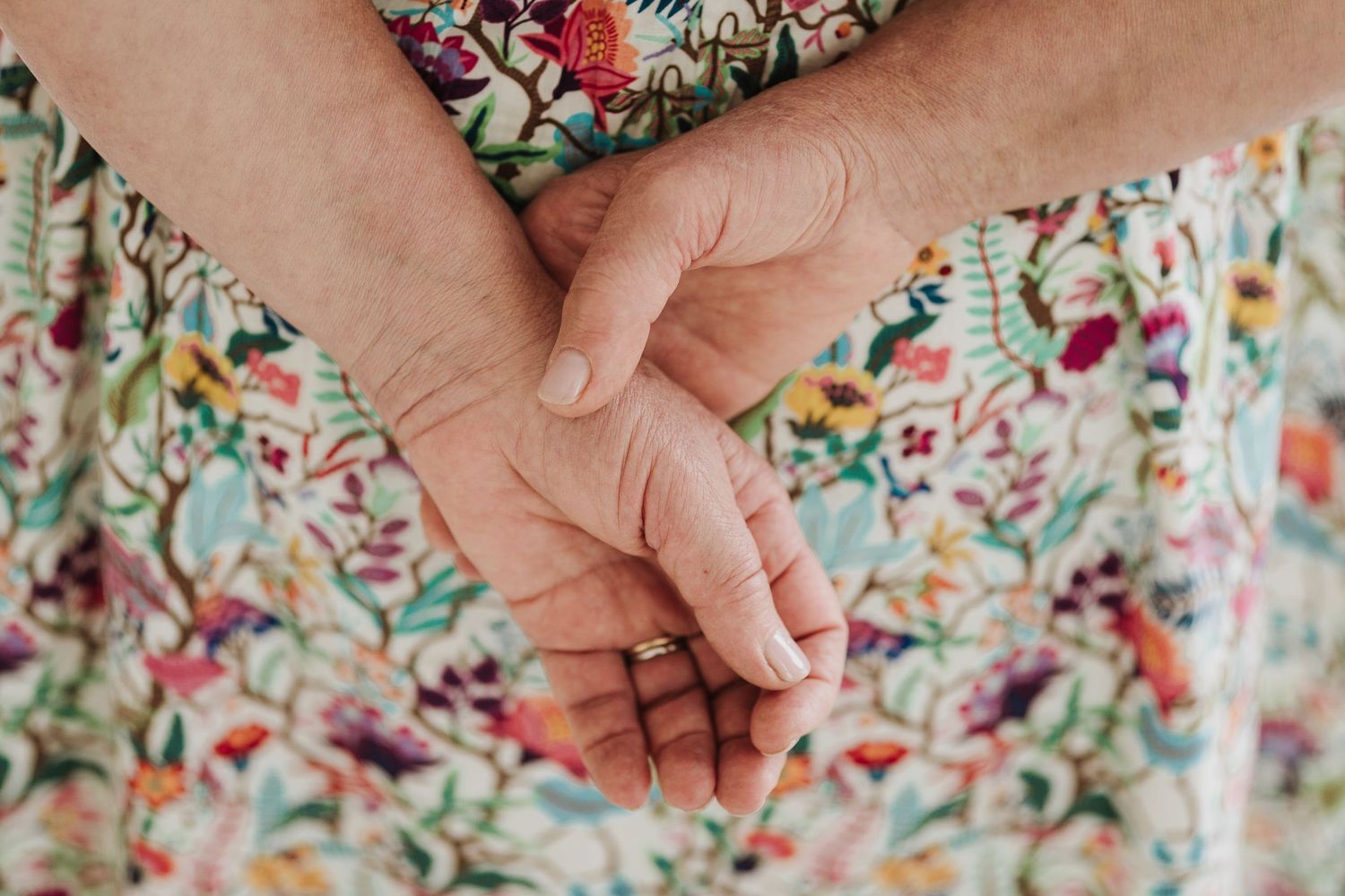 Close-up of hands clasped together against a floral patterned dress.