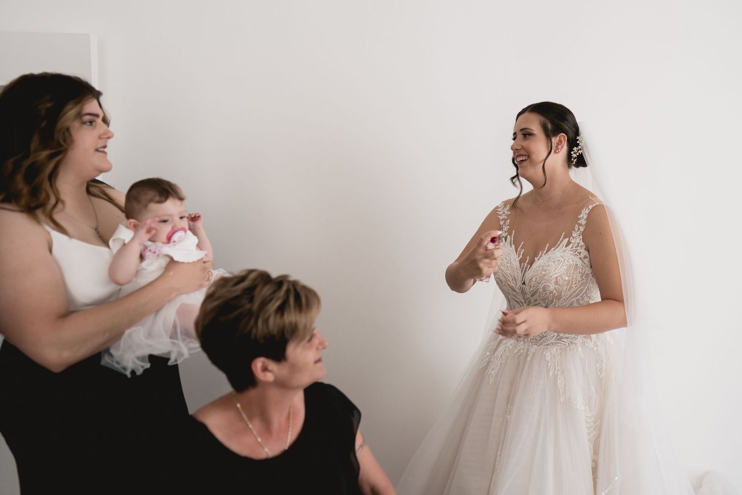Candid moment of joyful reactions during wedding preparations in a bright white room.