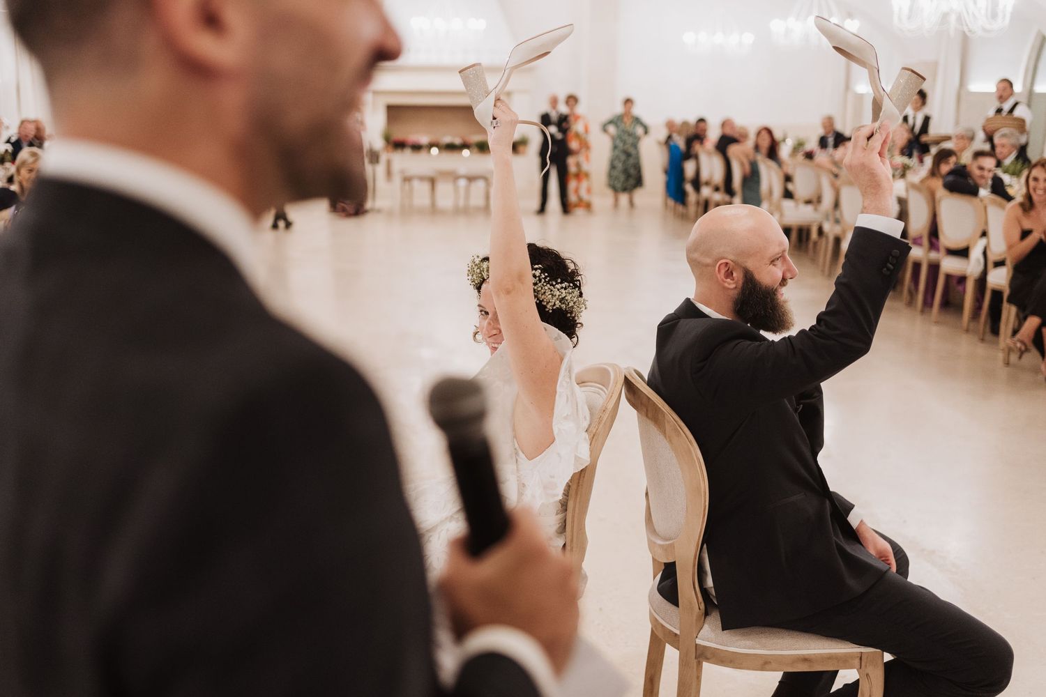 Wedding guests raise their hands in celebration during an indoor reception ceremony.