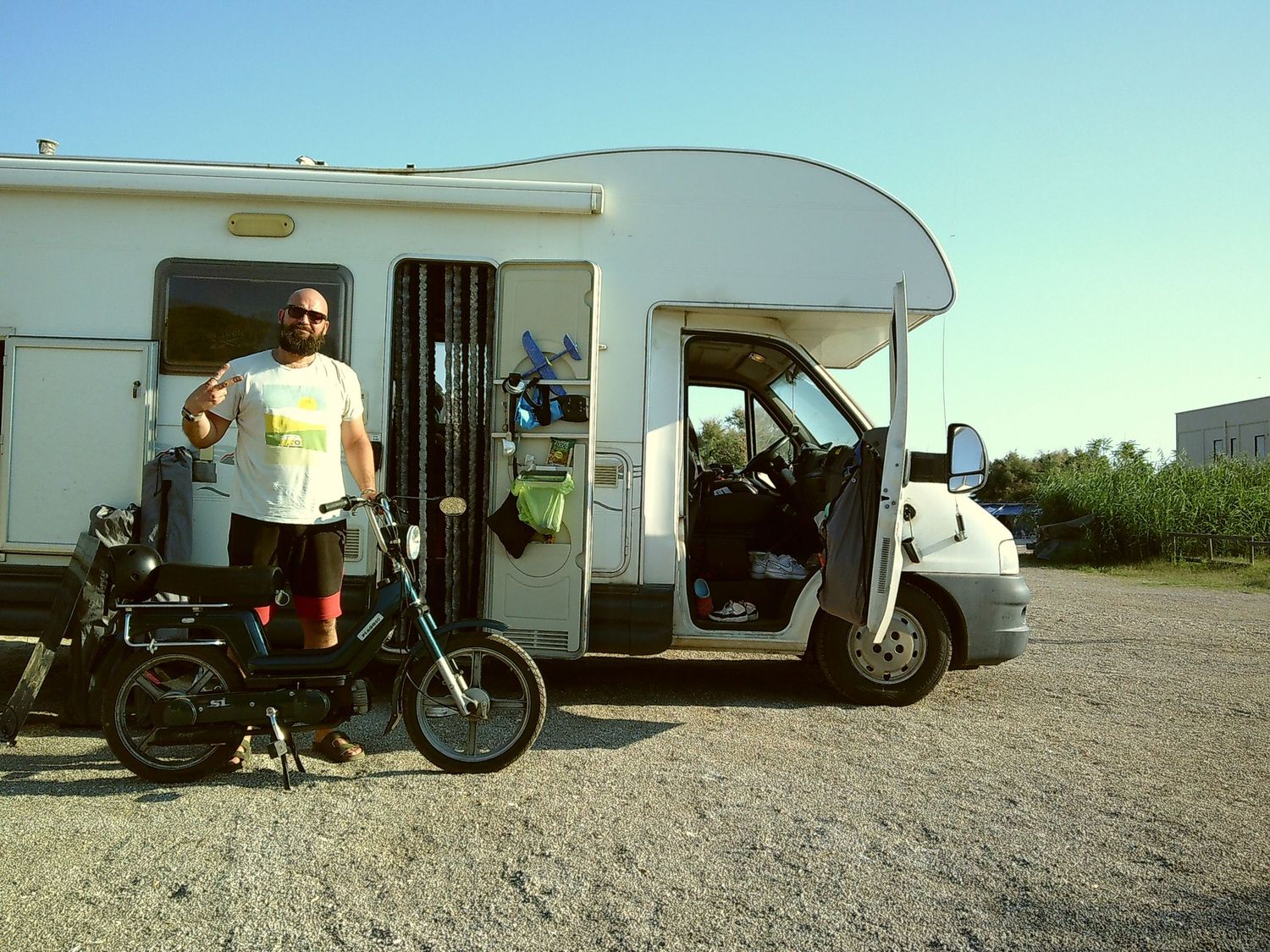 RV camper parked on gravel with a bicycle parked outside on a sunny day.