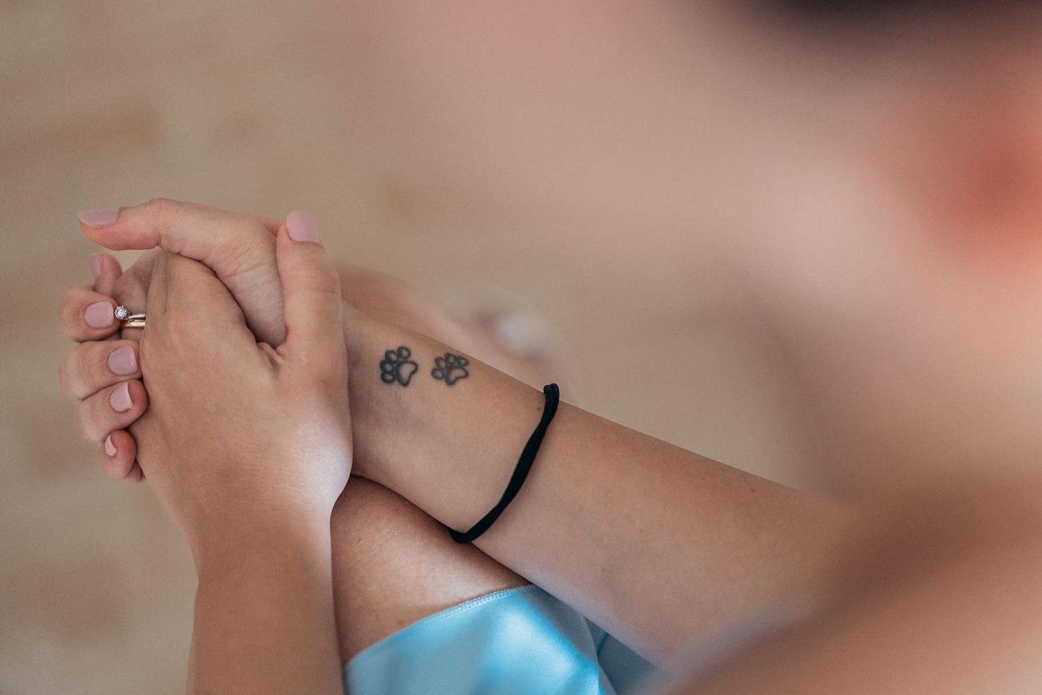 Closeup of clasped hands showing a black bracelet and tattoo in soft focus.
