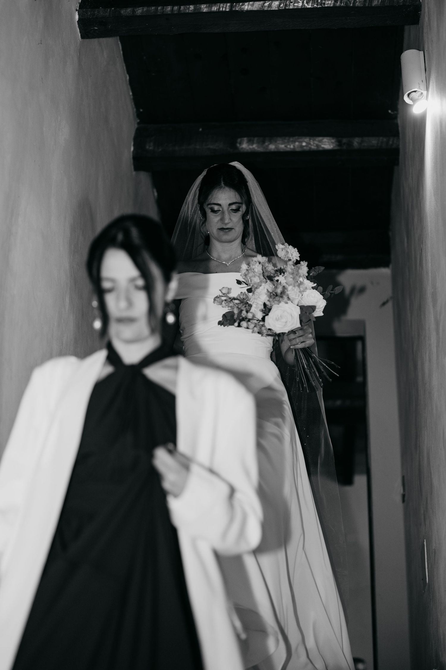 Artistic black and white photograph showing figures walking through a dimly lit hallway.