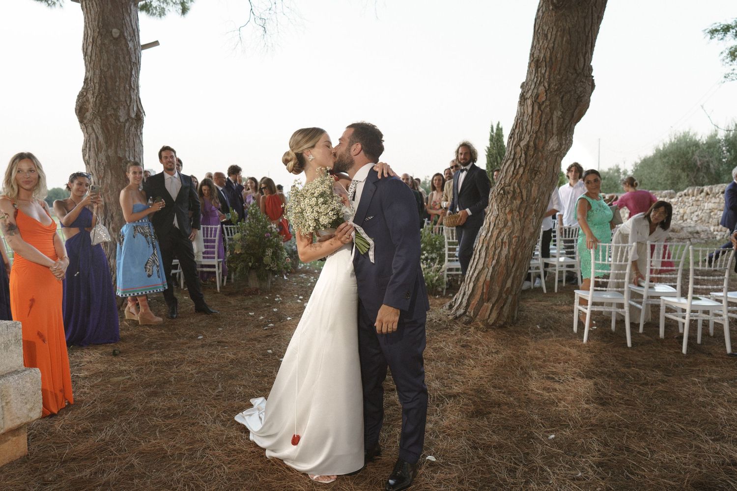 A wedding ceremony kiss in a rustic outdoor setting with guests watching.