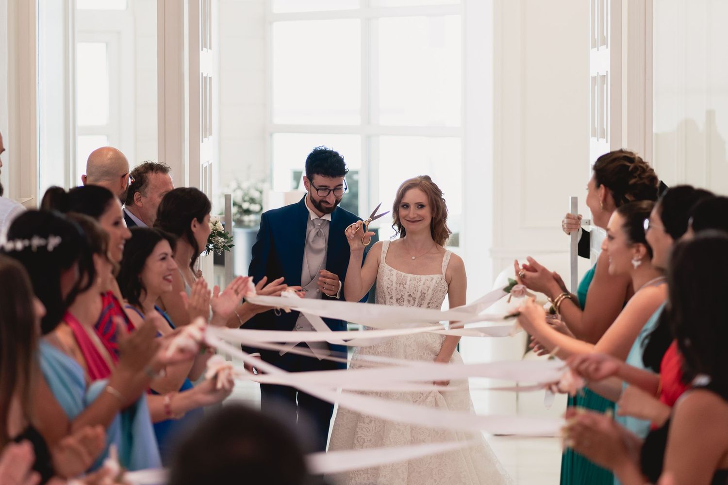 Wedding reception guests seated at white tables clapping during celebration.