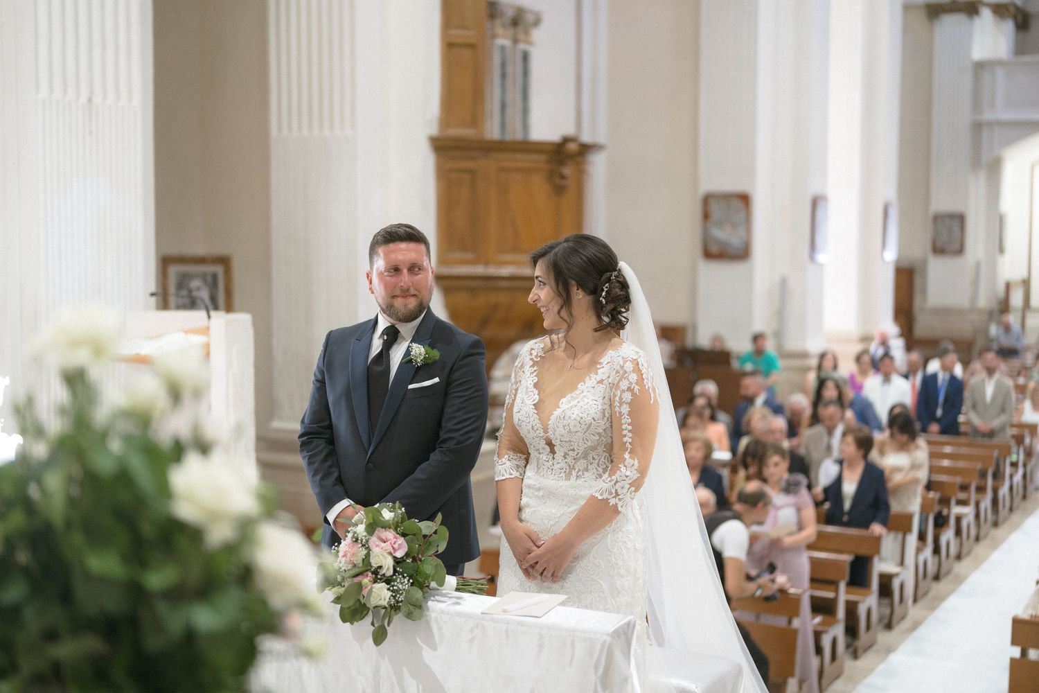 Traditional church wedding ceremony with white floral decorations and wooden pews.