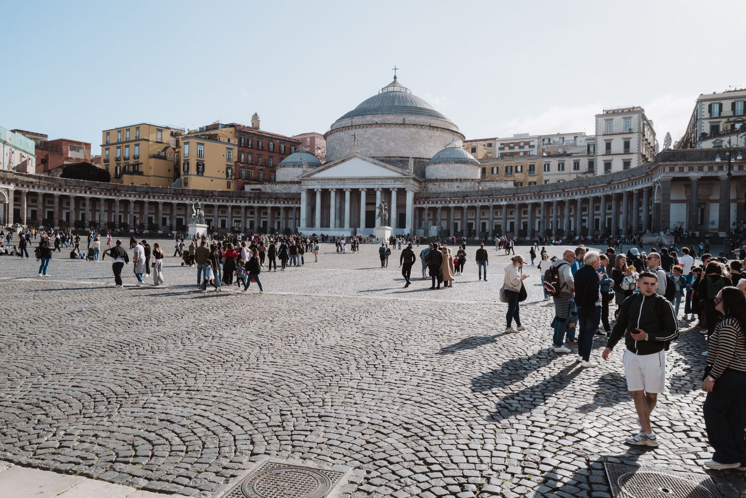 Piazza del Plebiscito in Naples with crowds gathering around the San Francesco di Paola church dome.