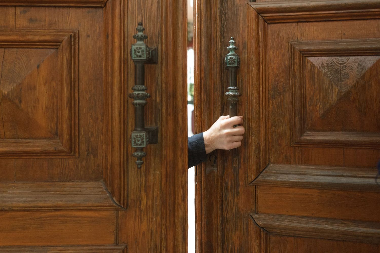 Person opening large ornate wooden double doors with decorative bronze handles at a church entrance.