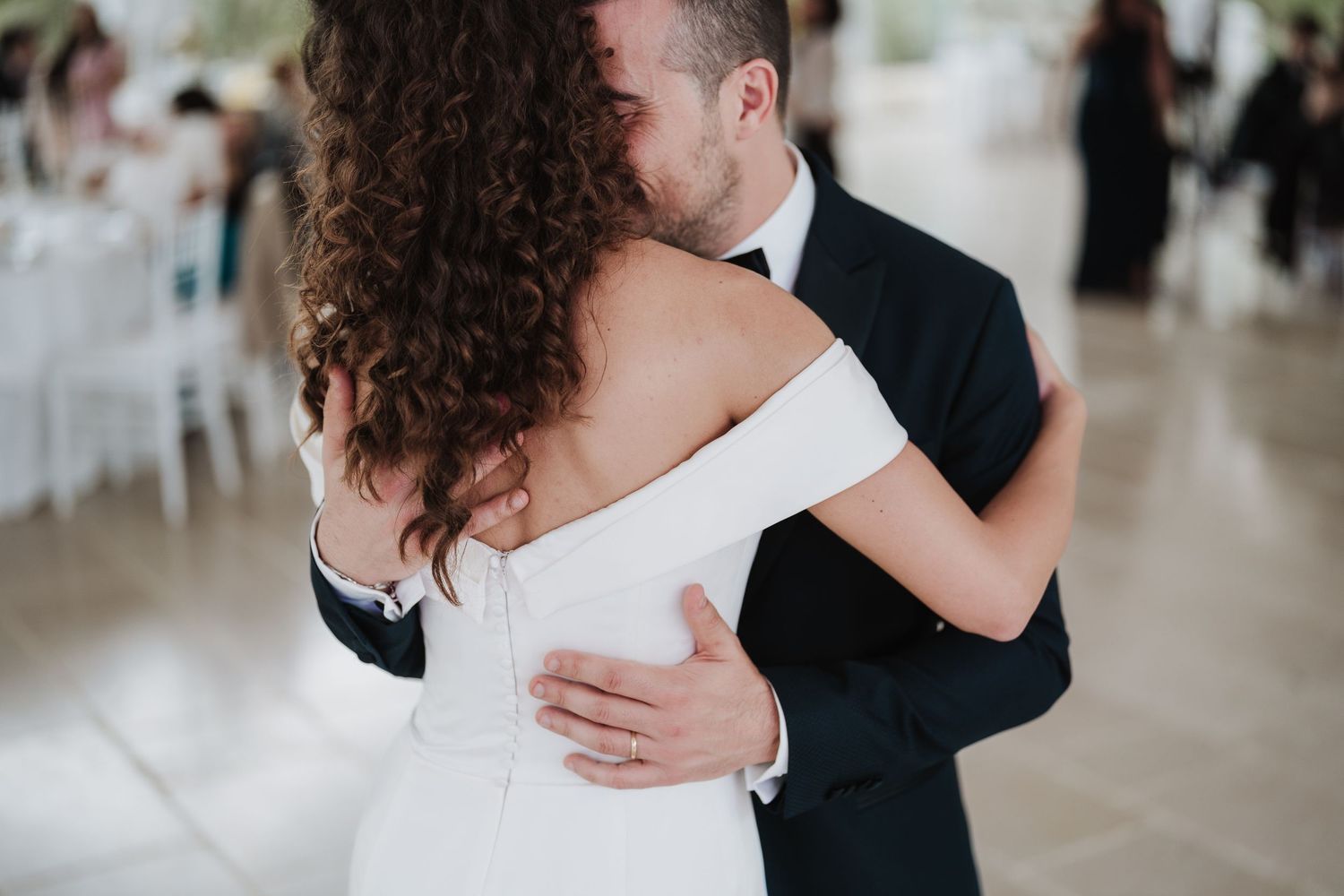 Couple dancing together at their wedding reception, bride in white off-shoulder gown.